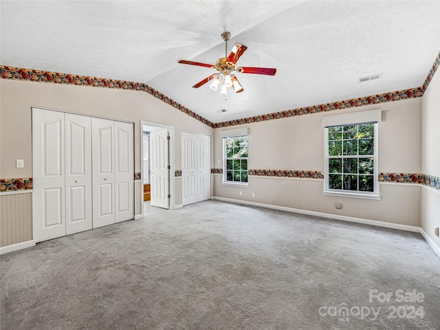 unfurnished bedroom with a textured ceiling, vaulted ceiling, multiple windows, and two closets