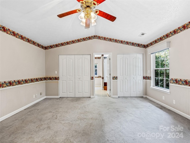 unfurnished bedroom with vaulted ceiling, ceiling fan, multiple closets, a textured ceiling, and carpet flooring