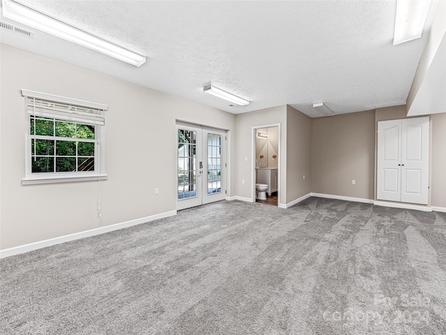 carpeted empty room with french doors and a textured ceiling