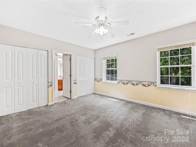 unfurnished bedroom featuring ceiling fan, multiple closets, carpet floors, and connected bathroom