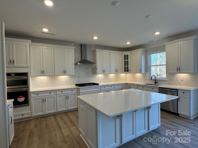 kitchen with white cabinets, appliances with stainless steel finishes, wall chimney exhaust hood, a kitchen island, and sink