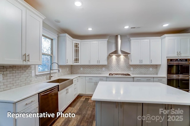 kitchen featuring appliances with stainless steel finishes, sink, white cabinets, and wall chimney range hood