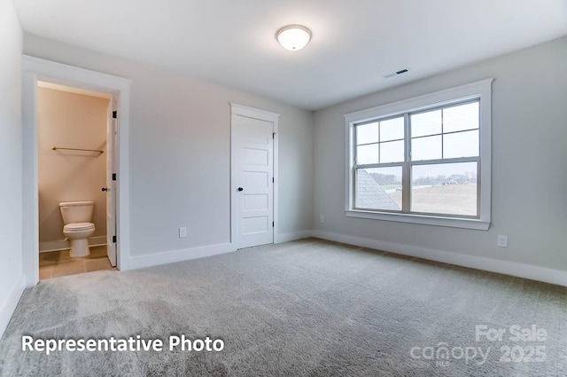 unfurnished bedroom featuring light colored carpet, a closet, and ensuite bath