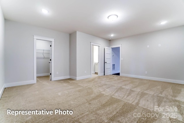 unfurnished bedroom with a spacious closet, a closet, and light colored carpet