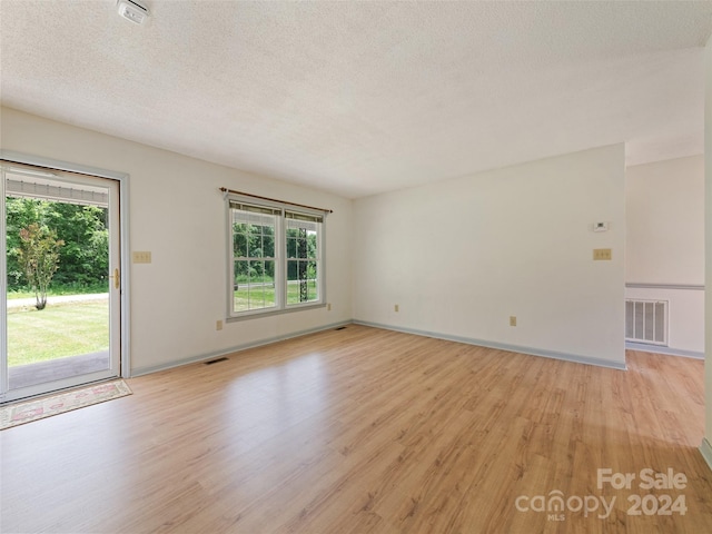 unfurnished room with a textured ceiling, light wood-type flooring, and a healthy amount of sunlight