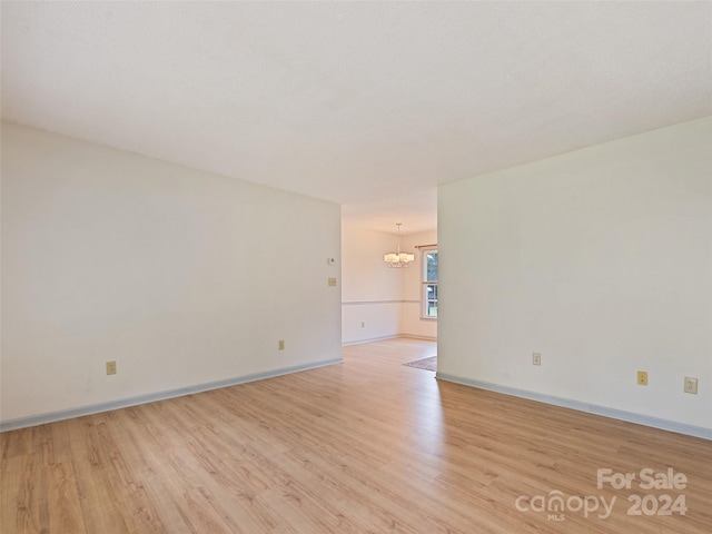 unfurnished room with a chandelier and light wood-type flooring