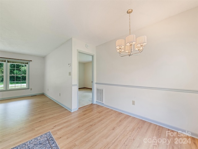 empty room with light hardwood / wood-style floors and a notable chandelier