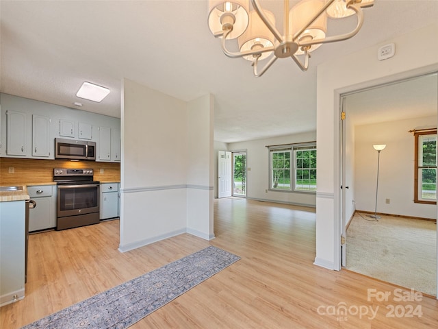 kitchen with hanging light fixtures, stainless steel appliances, light hardwood / wood-style flooring, backsplash, and a chandelier