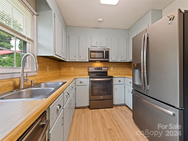 kitchen with sink, stainless steel appliances, light hardwood / wood-style floors, a textured ceiling, and decorative backsplash