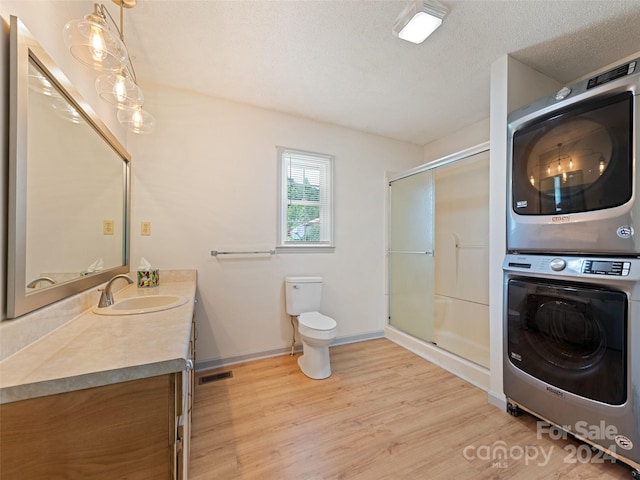 bathroom featuring hardwood / wood-style floors, vanity, stacked washer and clothes dryer, toilet, and a textured ceiling