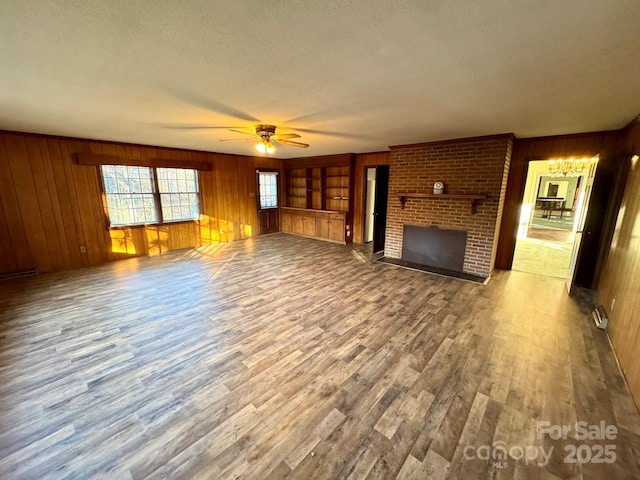 unfurnished living room with wood walls, wood-type flooring, a brick fireplace, a textured ceiling, and ceiling fan