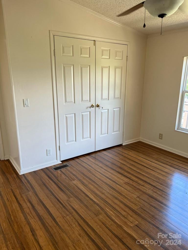 unfurnished bedroom featuring a textured ceiling, ceiling fan, a closet, and dark wood-type flooring