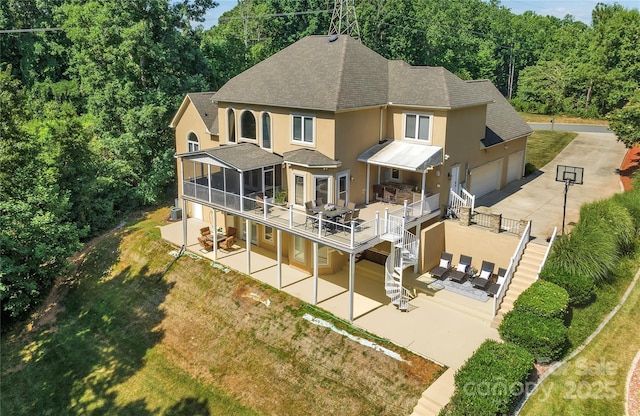 rear view of property featuring a sunroom, a deck, a patio area, and a garage