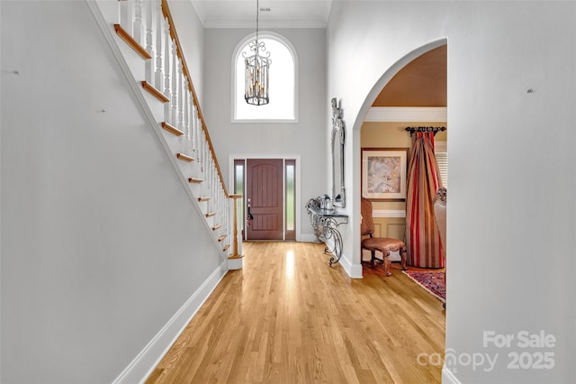 entrance foyer featuring crown molding, light wood-type flooring, and a high ceiling