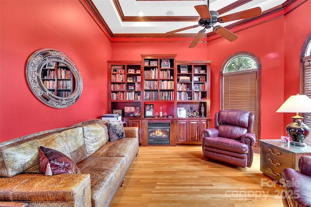 living room with crown molding, a raised ceiling, ceiling fan, and light wood-type flooring