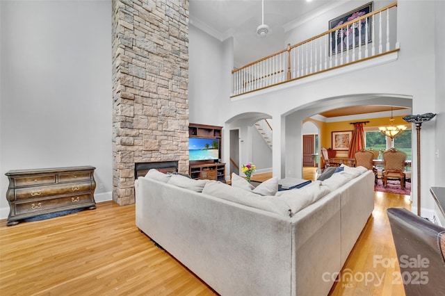 living room featuring crown molding, a stone fireplace, a chandelier, and light wood-type flooring