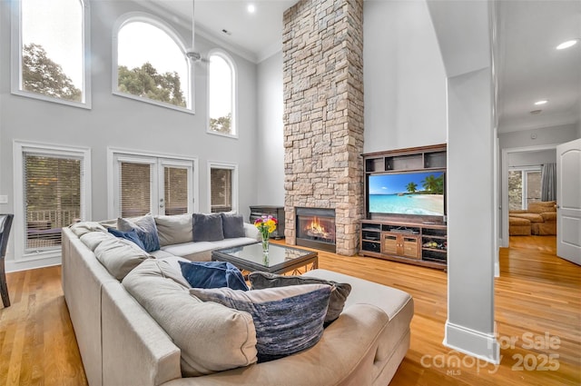 living room featuring crown molding, a fireplace, light hardwood / wood-style flooring, and a high ceiling