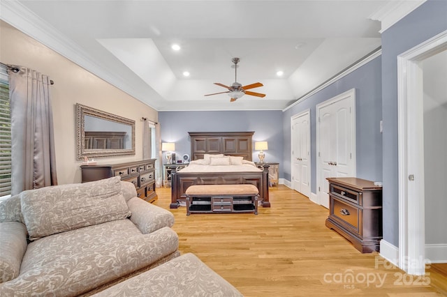 bedroom with light wood-type flooring, multiple closets, ornamental molding, a raised ceiling, and ceiling fan