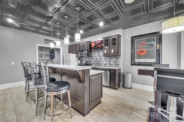 kitchen with appliances with stainless steel finishes, dark brown cabinets, light stone counters, tasteful backsplash, and a kitchen island