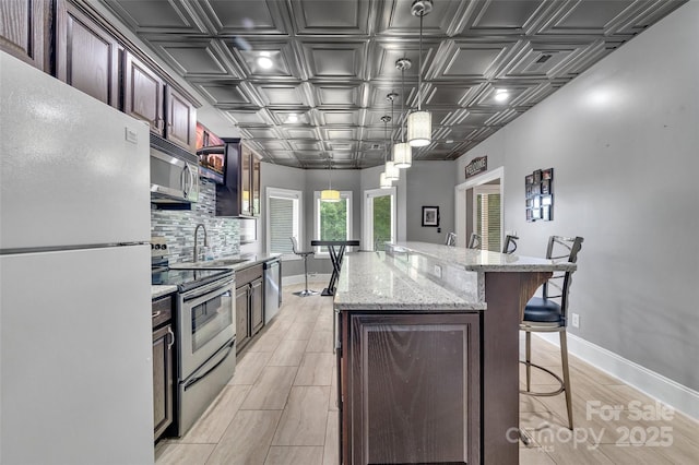 kitchen featuring appliances with stainless steel finishes, decorative light fixtures, a kitchen bar, decorative backsplash, and a center island