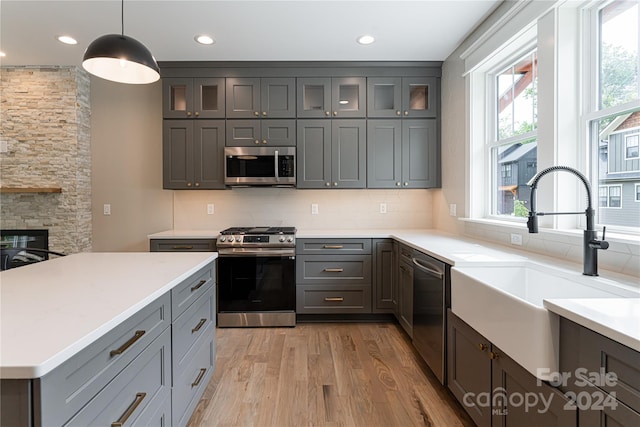 kitchen featuring decorative light fixtures, light hardwood / wood-style floors, sink, tasteful backsplash, and appliances with stainless steel finishes