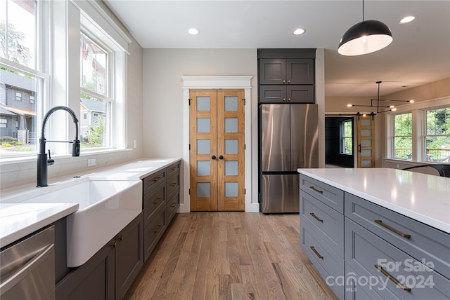 kitchen featuring appliances with stainless steel finishes, light hardwood / wood-style flooring, hanging light fixtures, light stone countertops, and sink