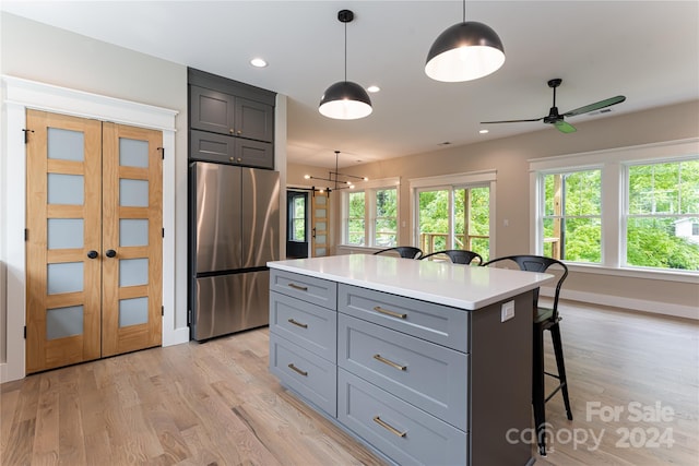 kitchen featuring light wood-type flooring, a kitchen island, decorative light fixtures, stainless steel fridge, and a breakfast bar area