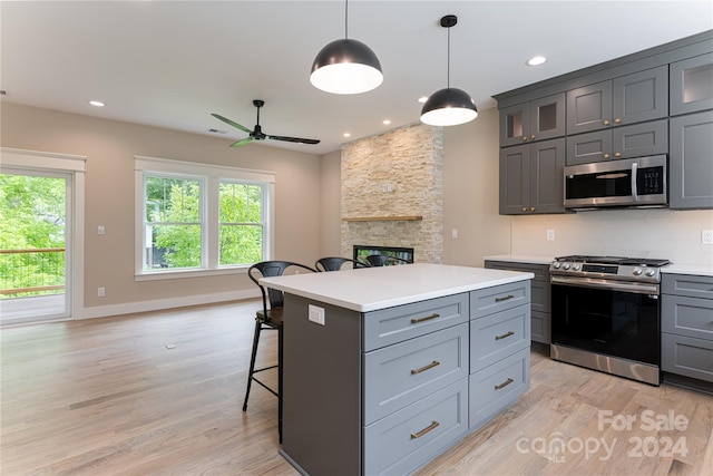 kitchen with light hardwood / wood-style flooring, stainless steel appliances, decorative light fixtures, a breakfast bar, and a kitchen island