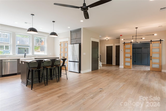 kitchen featuring appliances with stainless steel finishes, light wood-type flooring, a kitchen island, gray cabinetry, and a barn door