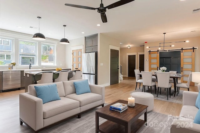 living room with ceiling fan, sink, light hardwood / wood-style floors, and a barn door