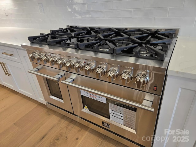 interior details featuring light hardwood / wood-style flooring, white cabinetry, double oven range, backsplash, and light stone counters