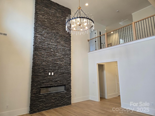 unfurnished living room featuring a high ceiling, a notable chandelier, a fireplace, wood-type flooring, and ornamental molding