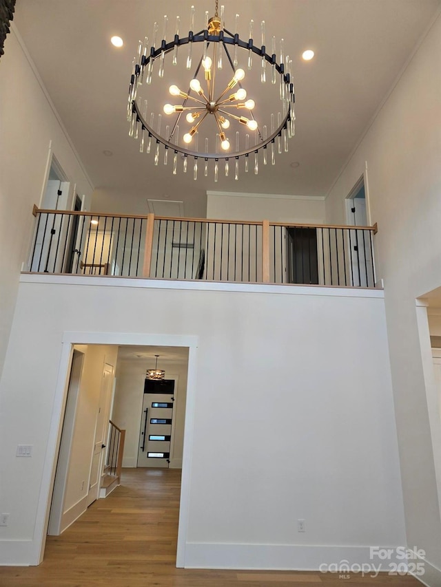 hall featuring ornamental molding, a towering ceiling, hardwood / wood-style floors, and a notable chandelier