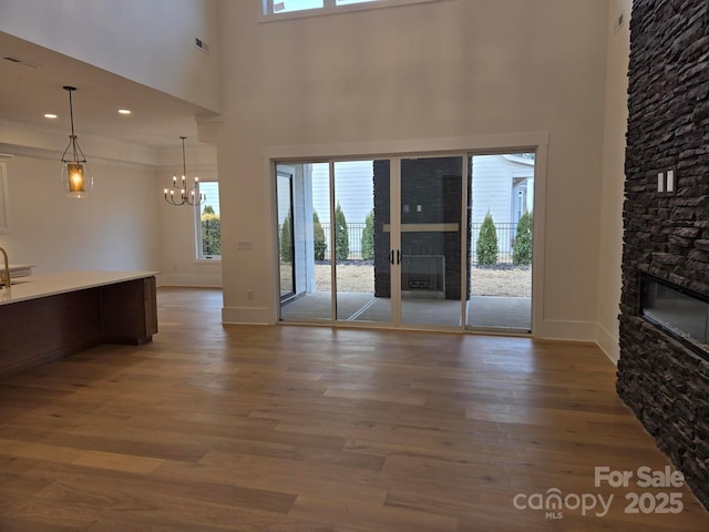 unfurnished living room with hardwood / wood-style flooring, a stone fireplace, a high ceiling, and a chandelier