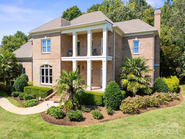 greek revival house featuring a balcony and a front lawn