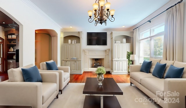 living room featuring built in shelves, a notable chandelier, crown molding, and light hardwood / wood-style floors