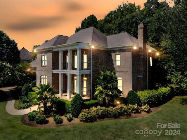 back house at dusk with a lawn and a balcony