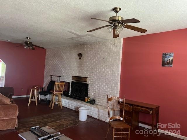 living room with ceiling fan, dark hardwood / wood-style flooring, a textured ceiling, and a brick fireplace