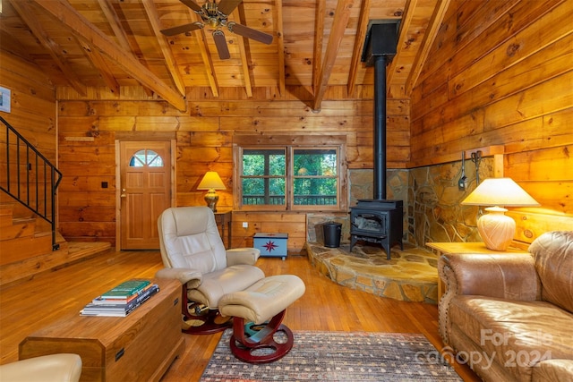 living room with wood ceiling, vaulted ceiling with beams, light hardwood / wood-style floors, a wood stove, and ceiling fan