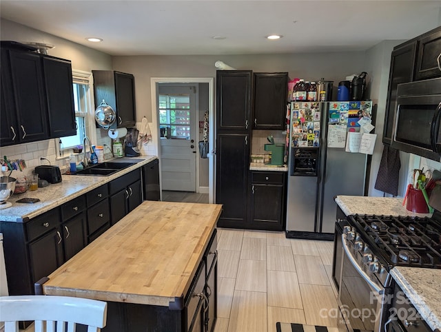 kitchen with tasteful backsplash, a kitchen island, sink, light stone countertops, and appliances with stainless steel finishes