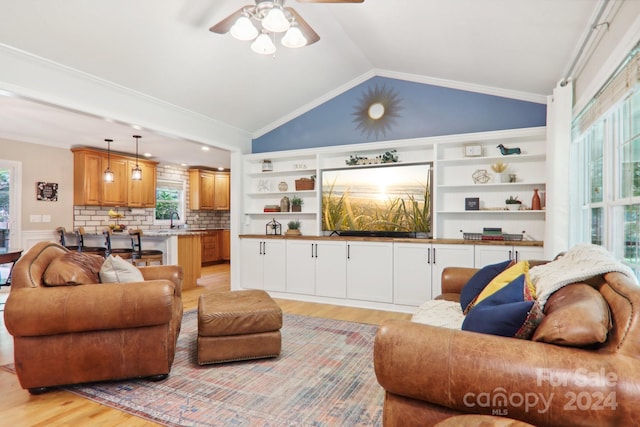 living room featuring light wood-type flooring, vaulted ceiling, crown molding, and sink