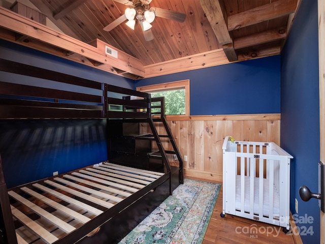 bedroom featuring wood ceiling, wood-type flooring, wooden walls, lofted ceiling with beams, and ceiling fan