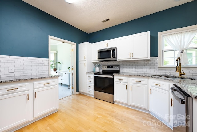 kitchen featuring light stone counters, a textured ceiling, stainless steel appliances, sink, and white cabinets