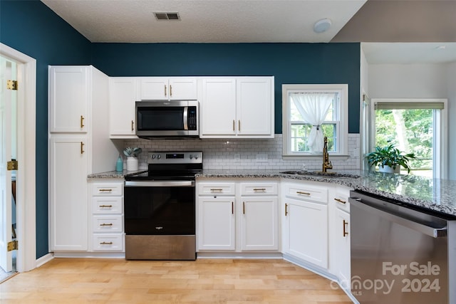 kitchen with light stone countertops, appliances with stainless steel finishes, decorative backsplash, sink, and white cabinetry