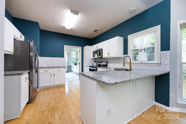 kitchen with kitchen peninsula, appliances with stainless steel finishes, light stone countertops, sink, and white cabinets