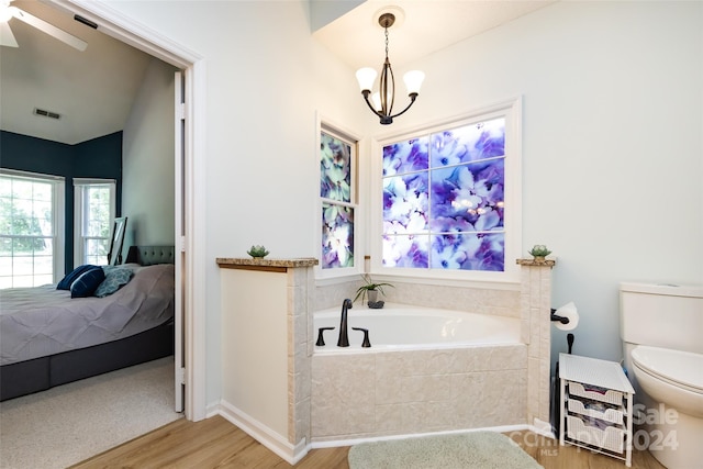 bathroom featuring ceiling fan with notable chandelier, wood-type flooring, a relaxing tiled tub, toilet, and lofted ceiling