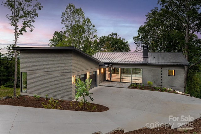 mid-century home featuring concrete driveway, a chimney, metal roof, an attached garage, and a standing seam roof