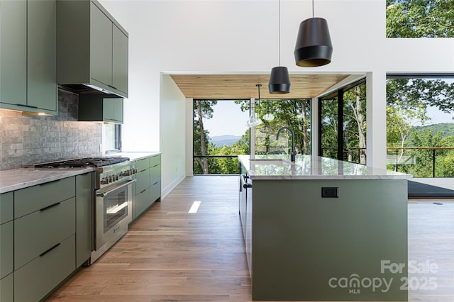 kitchen with high end stainless steel range oven, a center island with sink, a sink, and decorative light fixtures