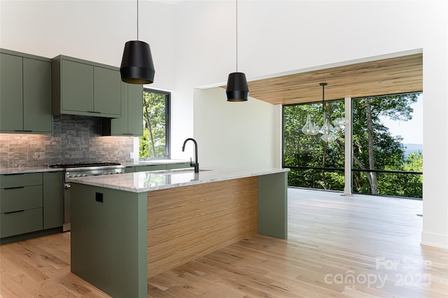 kitchen with decorative backsplash, an island with sink, light stone counters, high end stainless steel range oven, and a sink