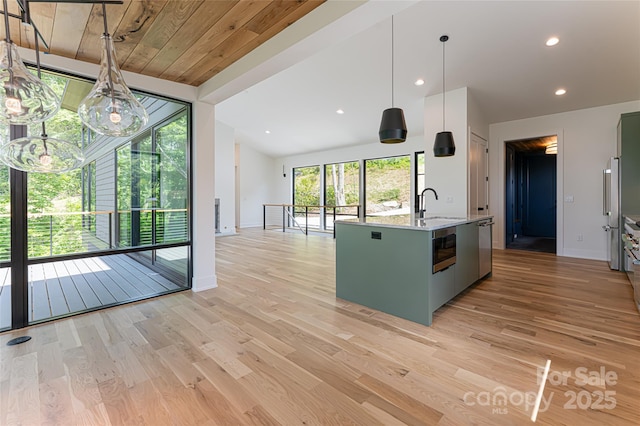 kitchen with light wood finished floors, stainless steel appliances, light countertops, a sink, and an island with sink